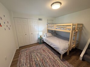 Ein Stockbett mit kleinem Tisch und Lampe, ein gemustertes Teppich und eine Tür mit Lüftung.