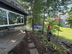 Un patio con mobiliario exterior, un sendero de piedra y vista a un jardín trasero con una chimenea y sillas.