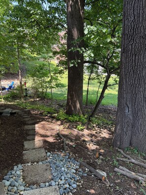 Un jardín con un sendero de piedra, árboles y una silla azul.