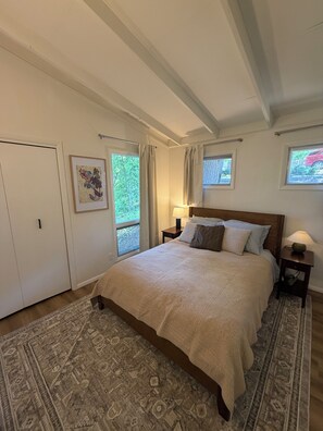 Un dormitorio con una cama grande, una mesita de noche, una ventana con cortinas y una puerta.
