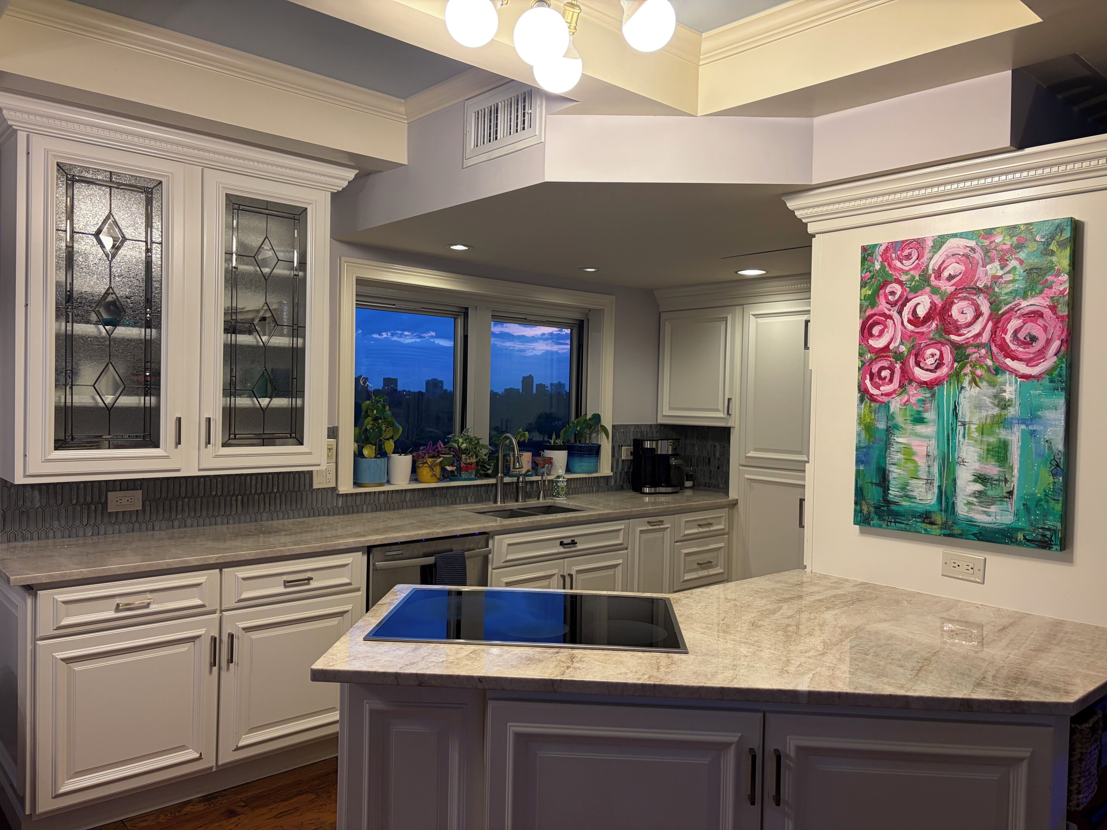 A modern kitchen with white cabinetry, a built-in island, and a cityscape view through the windows.