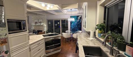 A modern kitchen with a built-in oven, microwave, and stainless steel appliances. There is a dining area with a glass table and chairs, and a large window providing a view of the cityscape.