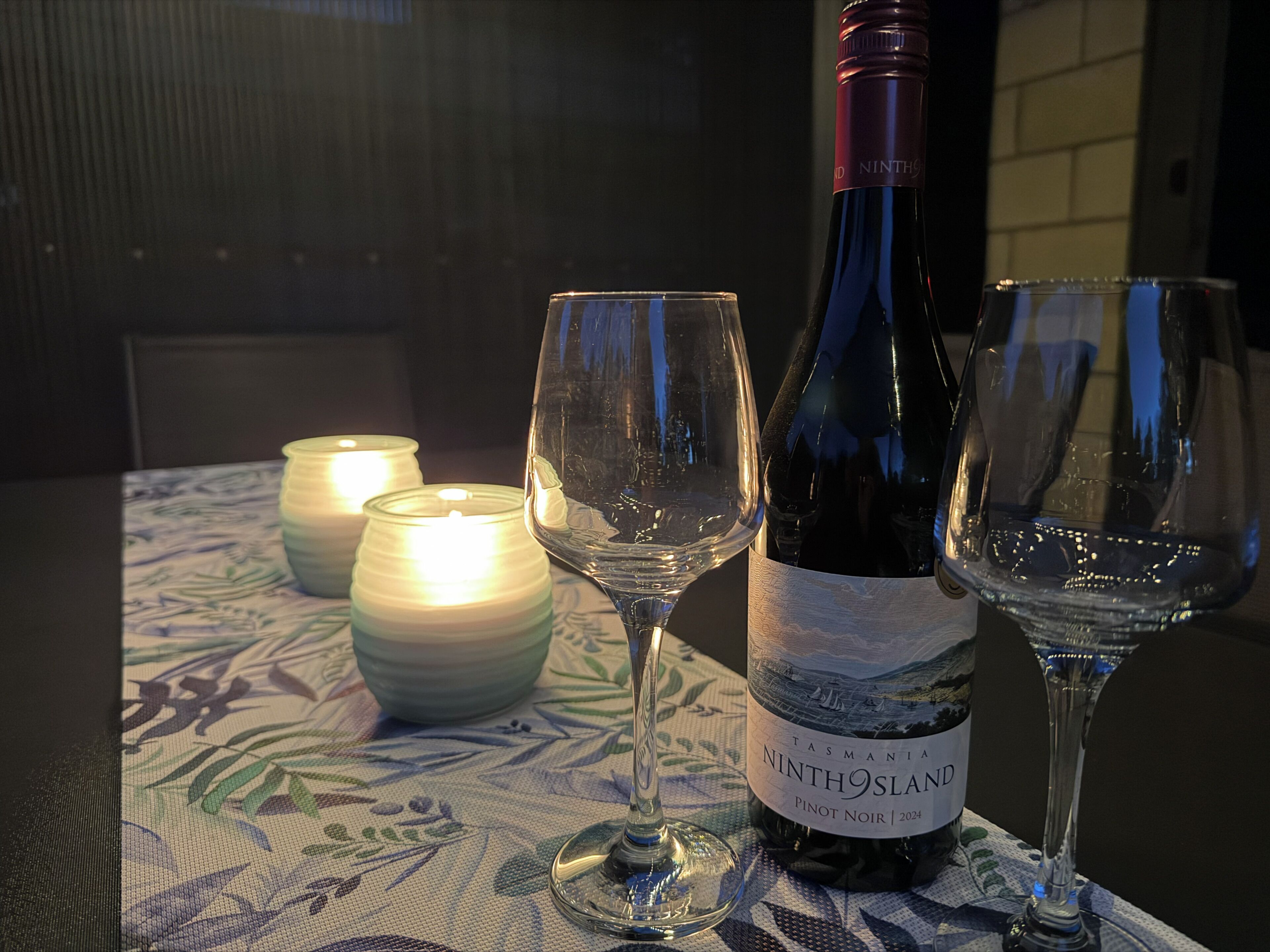 A bottle of wine, two glasses, and two candles on a table.
