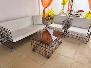 A modern outdoor seating area with a sofa and a glass-top coffee table, surrounded by potted plants.