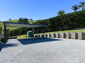 A covered outdoor area with a gravel surface, a green water tank, and a wooden fence.