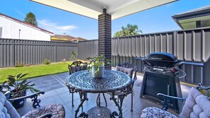 A patio with a round table, outdoor seating, a grill, and a fenced backyard. - Serenity Place - Relax, Unwind & Explore at Serenity Place (Mannering Park)