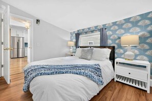 A bedroom with a bed, nightstands, and a view of a kitchen and dining area. - Cottage, Putting Green, Firepit, Walk to DT (St. Augustine)