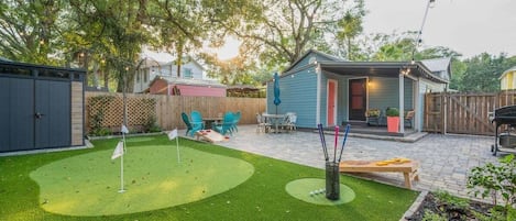 A backyard with a putting green, outdoor seating, and a small shed.