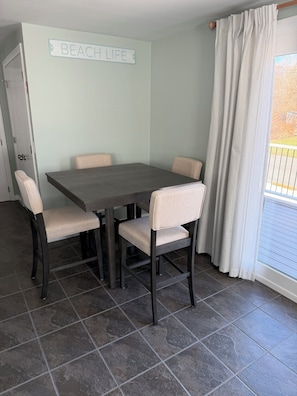 Uma área de refeições com uma mesa e quatro cadeiras, uma placa na parede com a inscrição 'BEACH LIFE' e uma janela com cortinas.