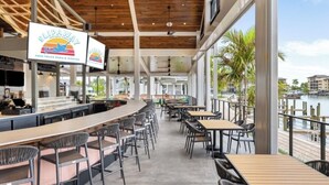 Un restaurante frente al agua con barra, mesas al aire libre y vistas al mar.