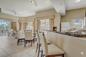 A spacious dining area with multiple chairs and tables, large windows with curtains, and a ceiling fan. - Disney Doorstep Resort Vibes Stay. (Orlando)