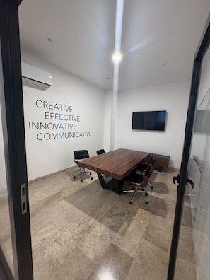 A conference room with a large wooden table, black chairs, a flat-screen TV on the wall, and a motivational quote on the wall. - Chic Queen Suite w 4 Rooftop Pools near 5th Ave (Playa del Carmen)