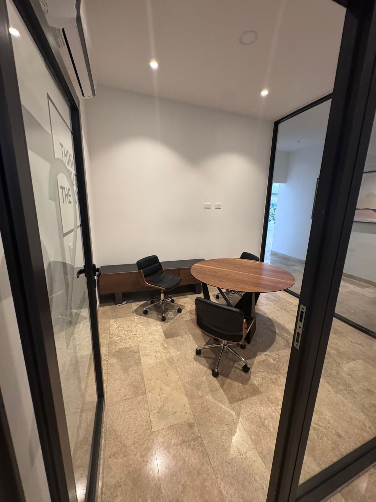A conference room with a glass partition, a wooden table, and two black office chairs.