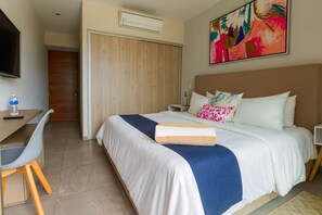 Habitación de hotel con cama, mesita de noche, escritorio con silla, televisor y un cuadro en la pared.