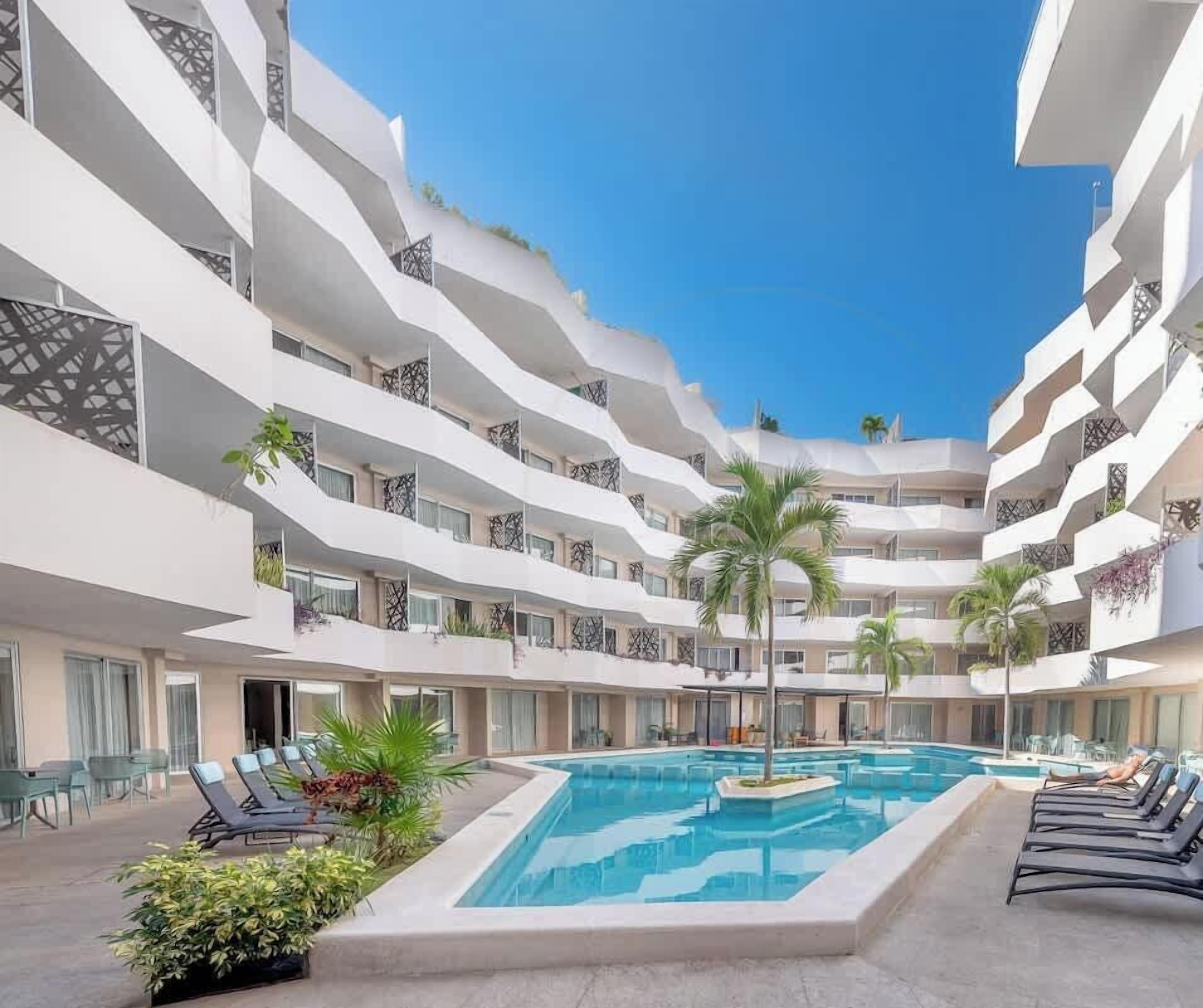 Ein mehrstöckiges Hotel mit einem zentral gelegenen Schwimmbad, Balkonen mit Bepflanzung und Liegestühlen.