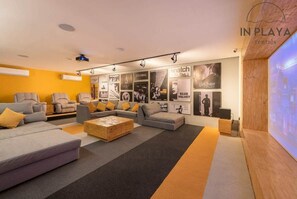 Una sala de estar moderna con sofás, una mesa de centro y una pantalla grande mostrando una película.