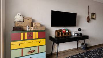 A room with a colorful dresser, a black desk with a flat-screen TV, and a bed with a patterned bedspread.