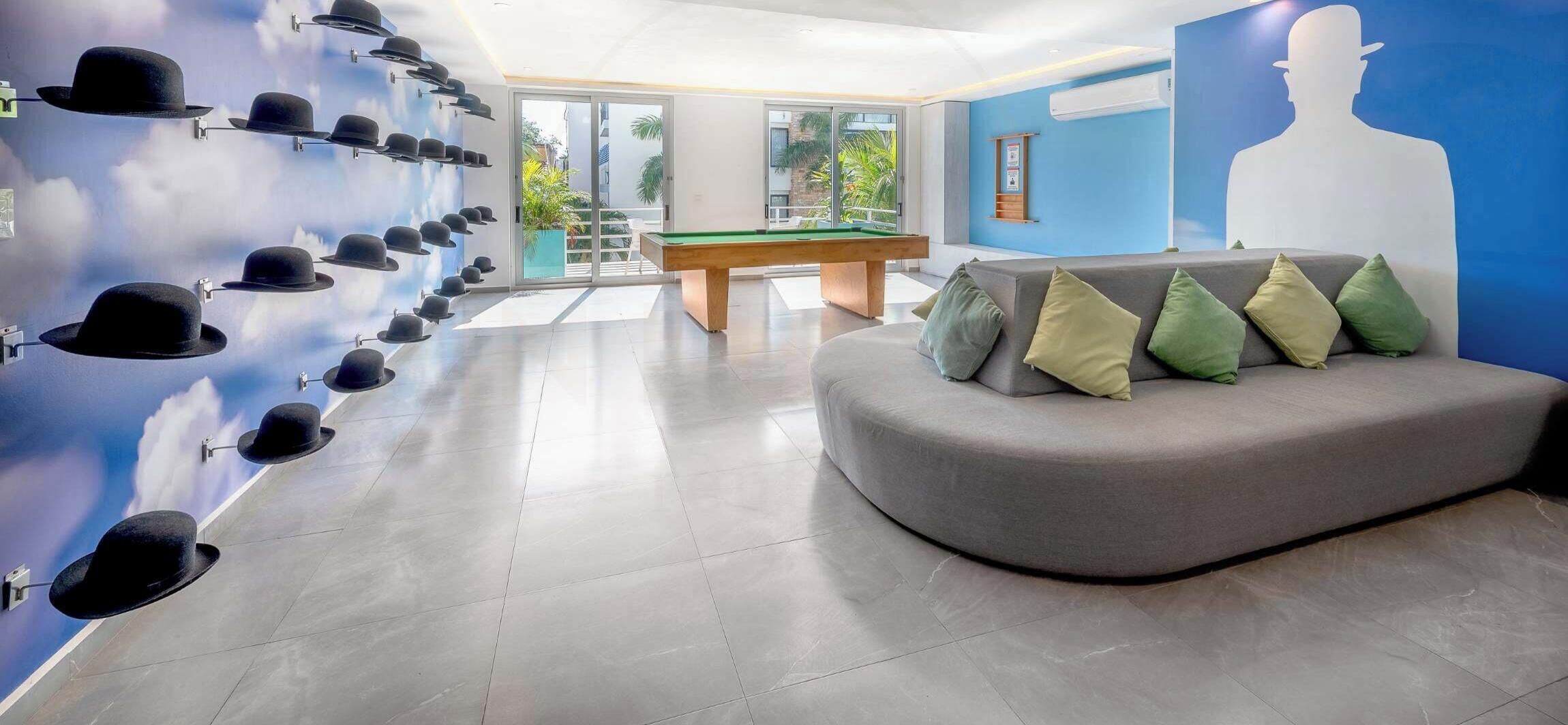 Un espace de détente moderne comprenant une table de billard, un canapé avec des coussins et un mur décoré de chapeaux.