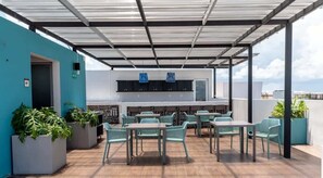 Eine Terrasse im Freien mit Tischen, Stühlen, einem Grillplatz und Blumentöpfen.