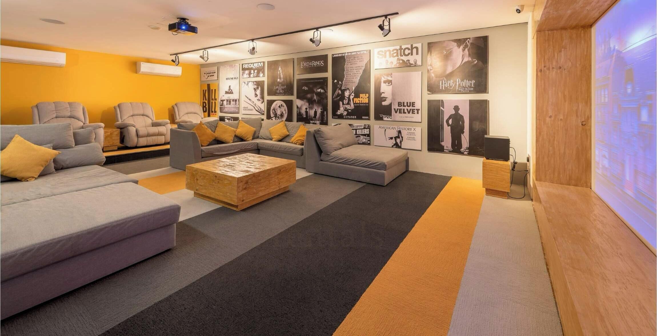 A modern lounge area with sofas, a coffee table, and a wall decorated with movie posters.