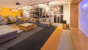 Ein modernes Wohnzimmer mit einer Eckcouch, einem Holztisch und einer großen Wand, die mit Filmplakaten dekoriert ist.