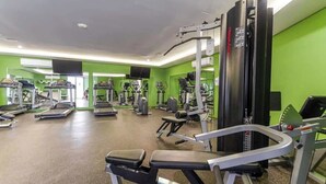 Et fitnesscenter med forskellig træningsudstyr, herunder løbebånd og styrkemaskiner, i et rum med grønne vægge.