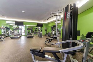 A gym with various exercise equipment, including treadmills and weight machines, in a room with green walls. - Stylish 1BR Condo w Rooftop Pool Near 5th Ave (Playa del Carmen)
