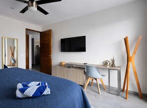 A bedroom with a bed, a desk, a chair, a television, and a wooden easel. - Stylish 1BR Condo w Rooftop Pool Near 5th Ave (Playa del Carmen)
