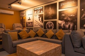 A modern living room with a sectional sofa, a wooden coffee table, and a wall adorned with movie posters. - Stylish 1BR Condo w Rooftop Pool Near 5th Ave (Playa del Carmen)