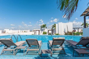 A pool area with lounge chairs, a clear blue sky, and palm trees. - Stylish 1BR Condo w Rooftop Pool Near 5th Ave (Playa del Carmen)