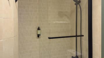 Een douchegedeelte met een glazen deur, een handdouche en een shampoo flacon aan de muur.