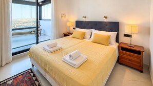 Une chambre d’hôtel avec un grand lit, deux tables de chevet, une vue à travers une porte vitrée et un tapis à motifs.