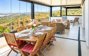 A dining area with a table set for six, surrounded by wicker chairs with red cushions, overlooking a scenic landscape. - Amazing apartment in Estepona with swimming pool (Estepona)
