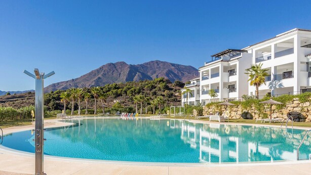 Une piscine entourée d’un paysage montagneux, un bâtiment blanc doté de balcons et des palmiers.