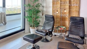 Une pièce moderne avec deux fauteuils en cuir noir, une petite table ronde, un grand lampadaire et une grande plante en pot.