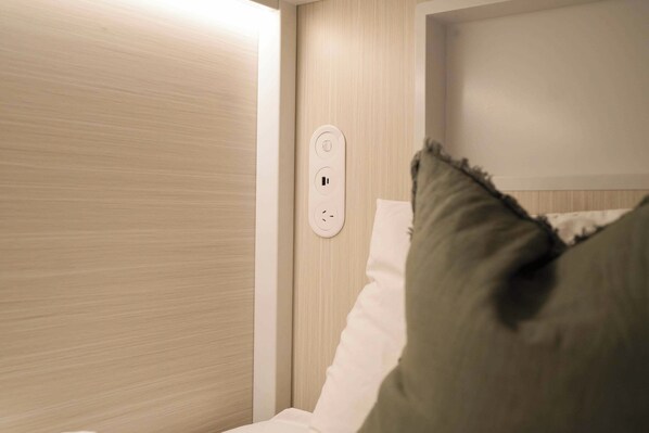 A hotel room with a wooden panel wall, a white bed with a pillow, and a power outlet on the wall.