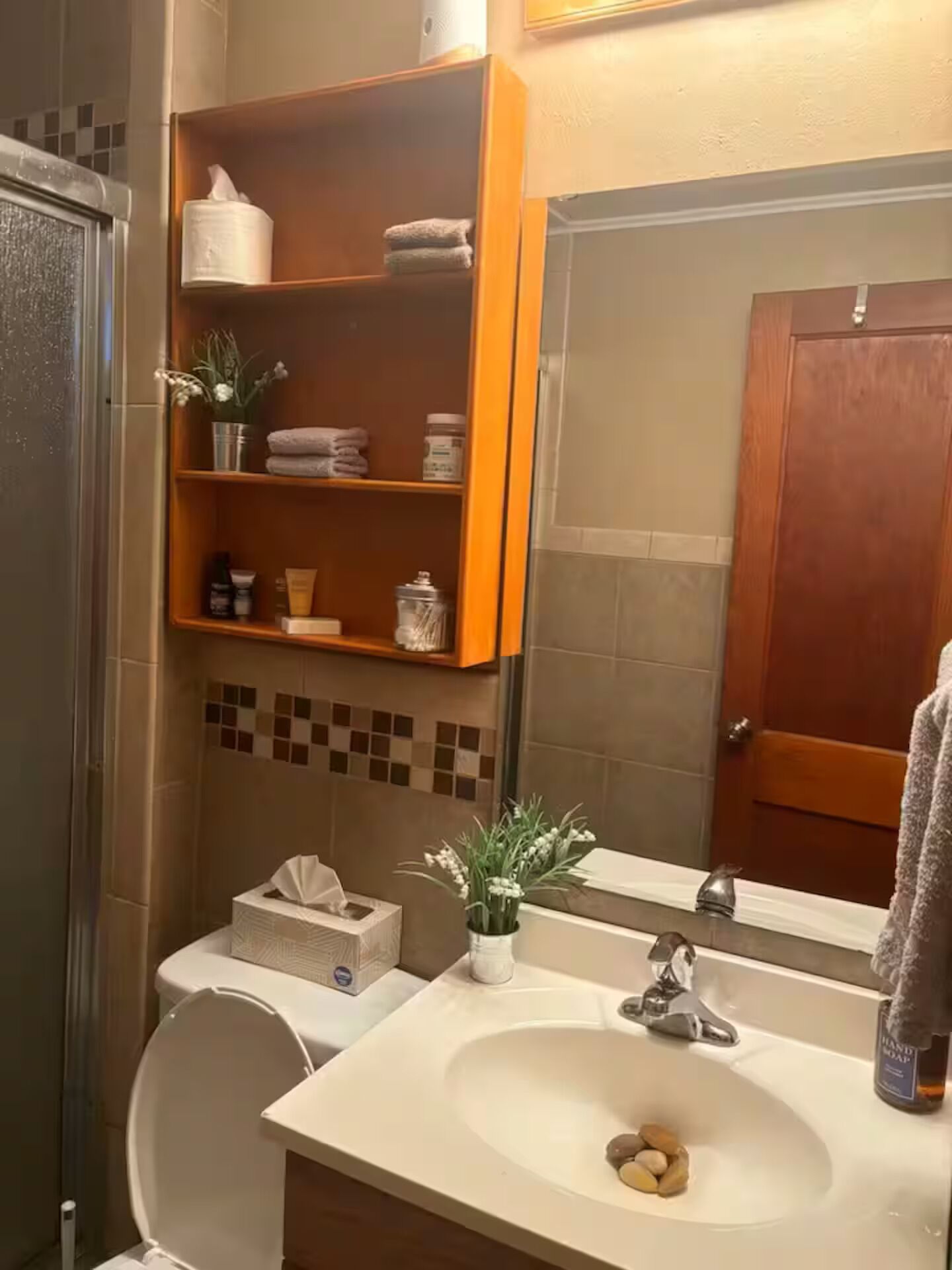 Et badeværelse med vask, spejl og hylder med toiletartikler.