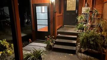 Entrada de una casa de madera con una puerta oscura, escalones que conducen a un porche y plantas en macetas.
