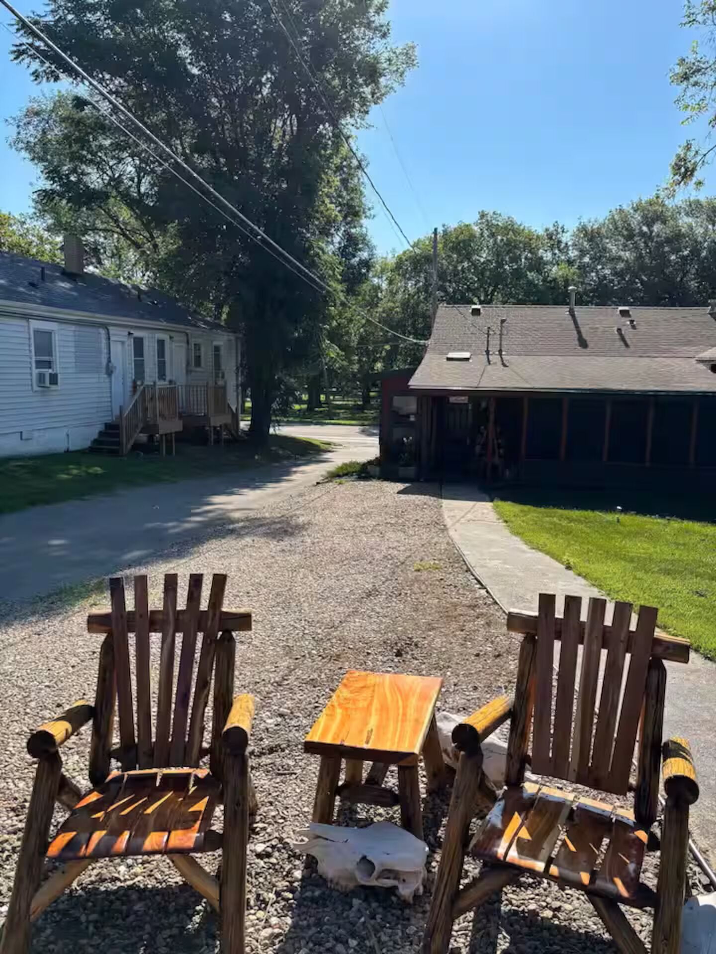 A gravel driveway leading to a house with two wooden chairs and a small wooden table.