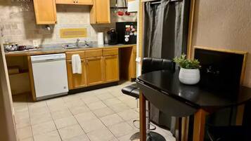 Una cocina compacta con armarios de madera, lavavajillas, cafetera y una pequeña mesa de comedor con planta en maceta.