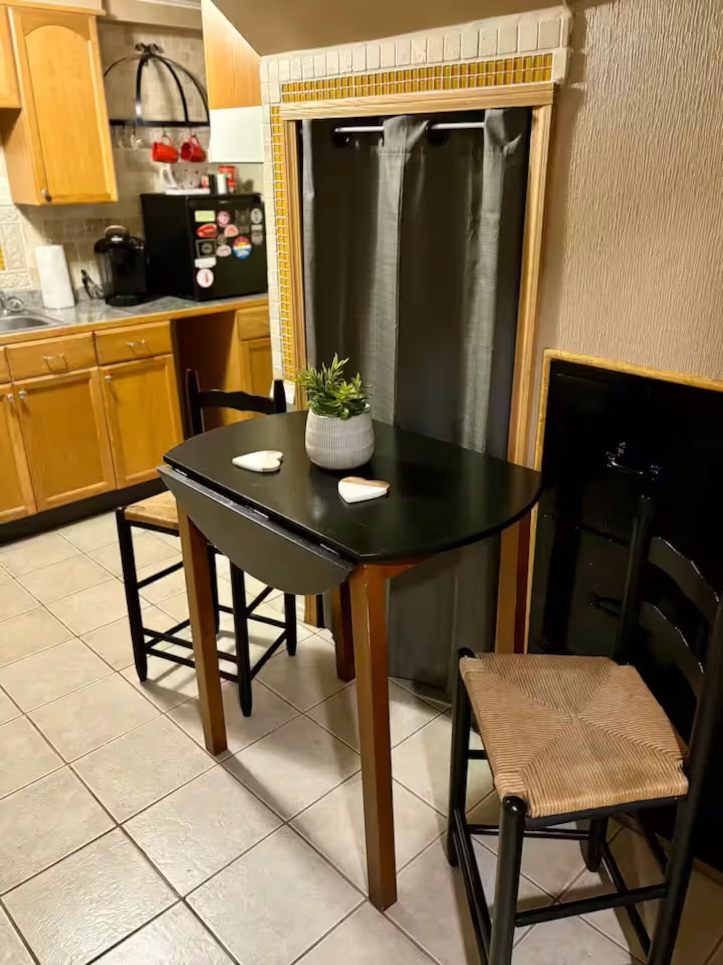 Una cocina compacta con una mesa de comedor, sillas, un refrigerador y una pequeña planta en maceta.