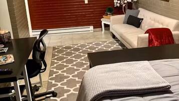 Un dormitorio con cama, escritorio, silla, sofá y una pequeña mesa con una planta.