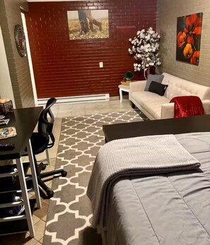 Un dormitorio con cama, escritorio, silla, sofá y una pequeña mesa con una planta.