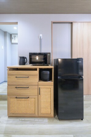 A kitchenette with a microwave, a black refrigerator, wooden cabinets, and a coffee maker. - Shinjuku 6-chome City Stay 1F (Shinjuku)