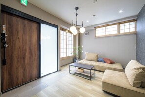 A modern interior with a wooden door, a sofa set, a coffee table, and a large window with natural light. - Shinjuku 6-chome City Stay 1F (Shinjuku)