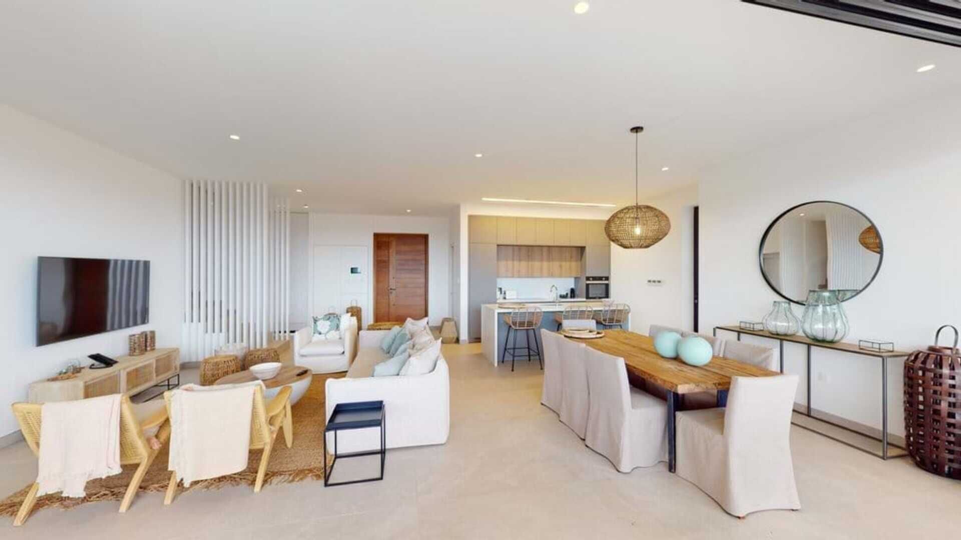 A modern living room with a flat-screen TV, a dining area with a wooden table, and a kitchen in the background.