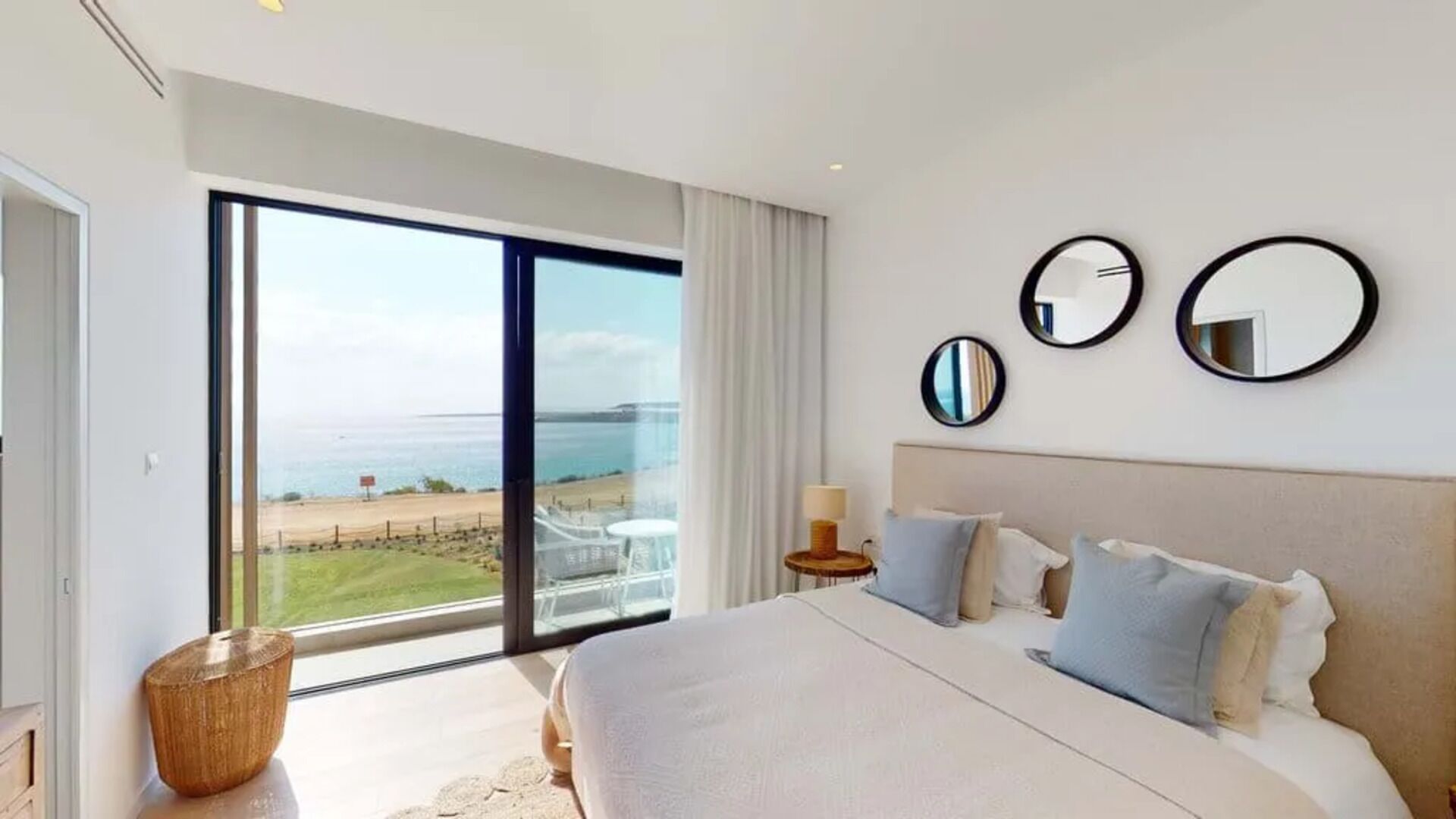 A hotel room with a large bed, a view of the beach, and three round mirrors on the wall.