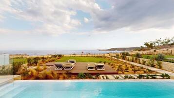 A poolside view with a clear sky, a beach in the distance, and a well-maintained lawn with lounge chairs.