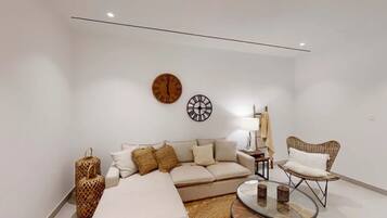 A modern living room with a sofa, a chair, a coffee table, and two wall clocks.