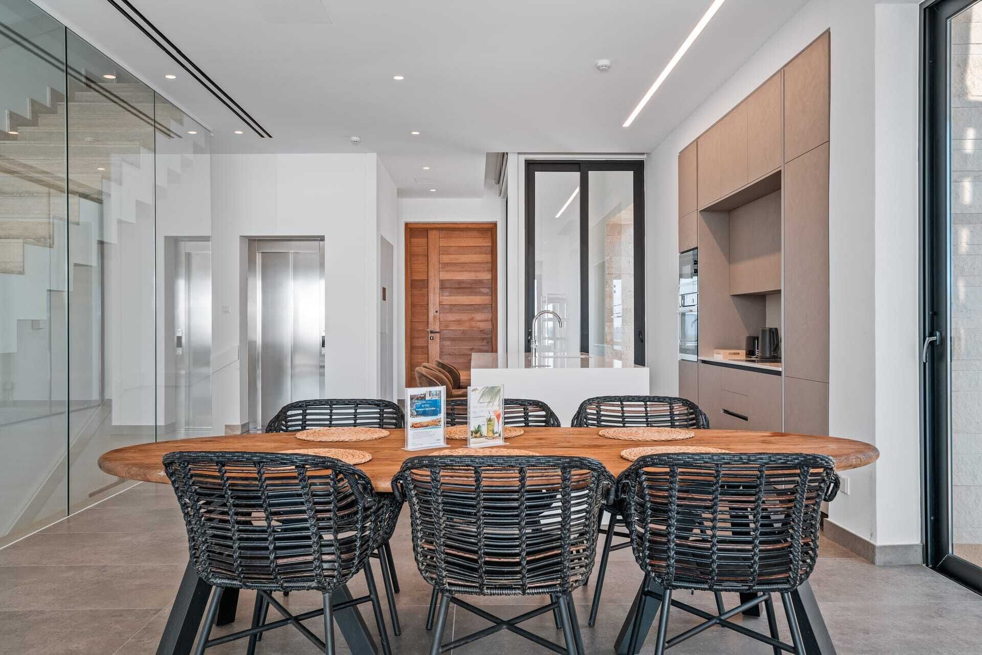Un espace repas moderne avec une table ronde, six chaises en rotin noir et une cloison en verre.